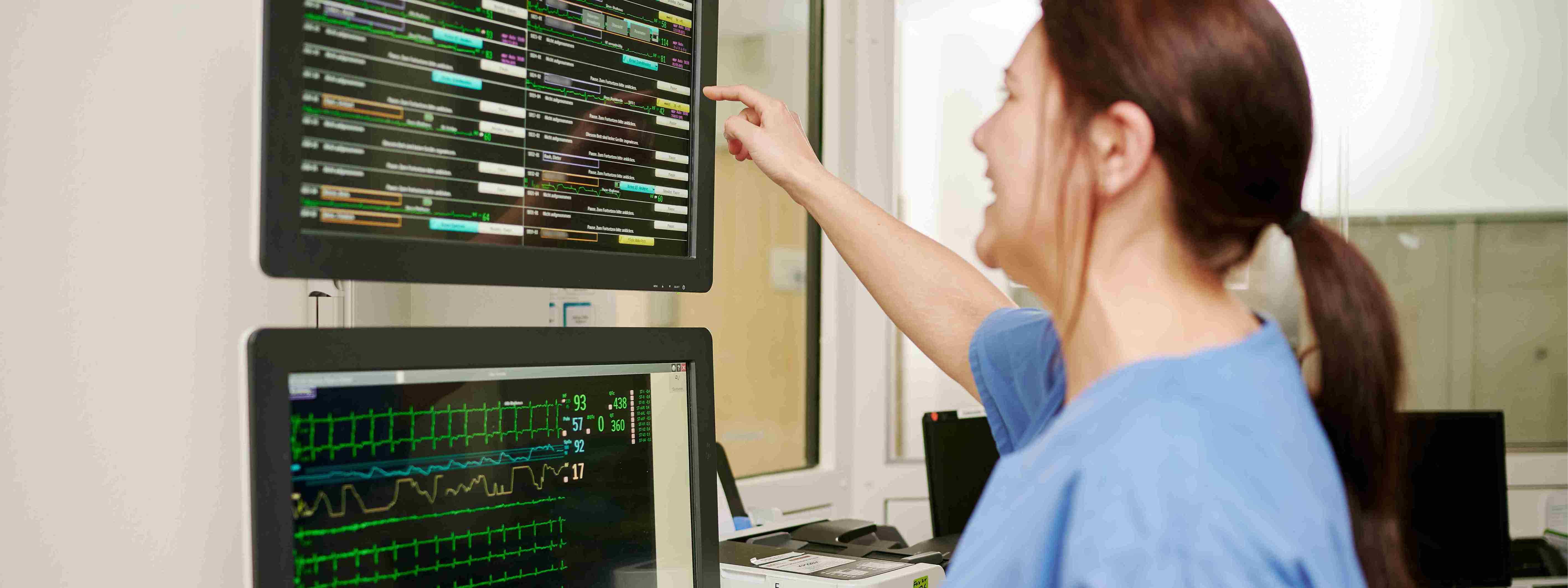 Das Bild zeigt eine Pflegefachkraft an den Monitoren im Stationszimmer der Intenivstation